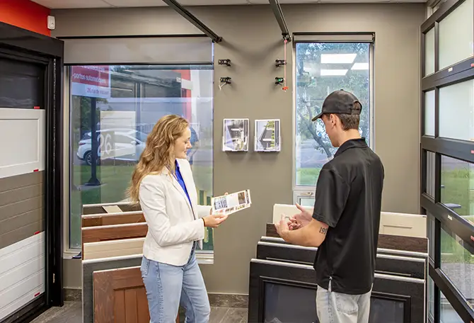 Des clients examinant des échantillons de portes de garage GARAGA dans une salle de montre, comparant les styles de panneaux, les couleurs et les matériaux avant l’installation.