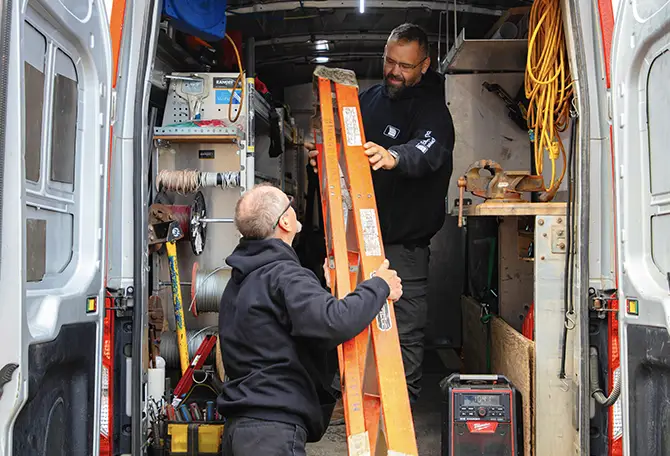 Deux techniciens travaillent ensemble pour décharger une échelle d’un véhicule de service.
